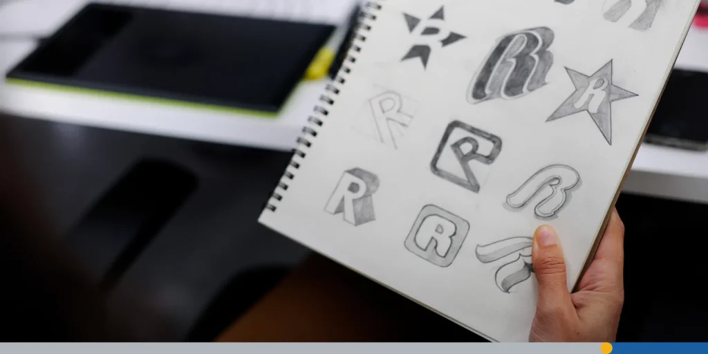 Hand holding a notebook full of logo design concepts.