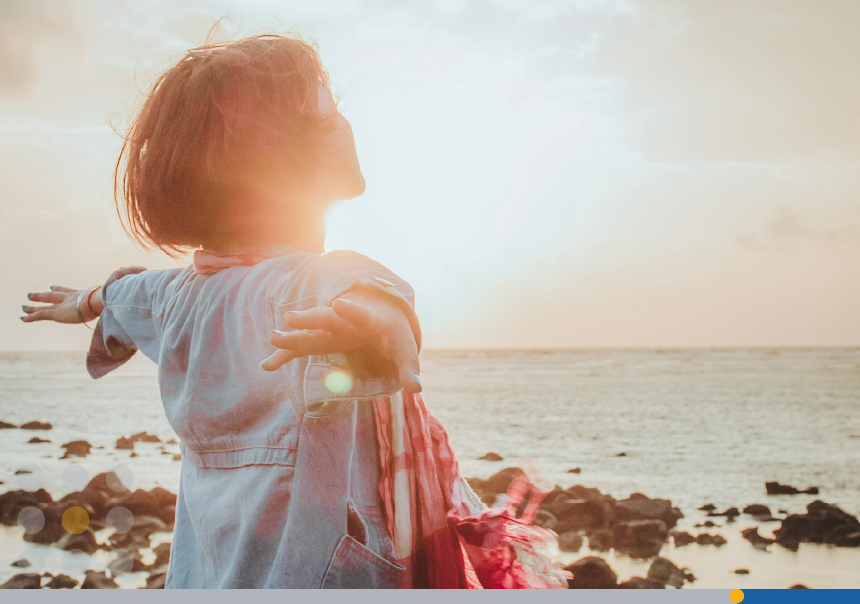 The sun shines on a woman standing on a beach.