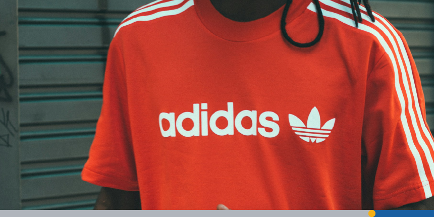 A man wears a red t-shirt with the distinctive Adidas logo design and font.